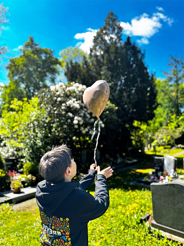 Ein Junge lässt auf einem Friedhof einen Luftballon steigen